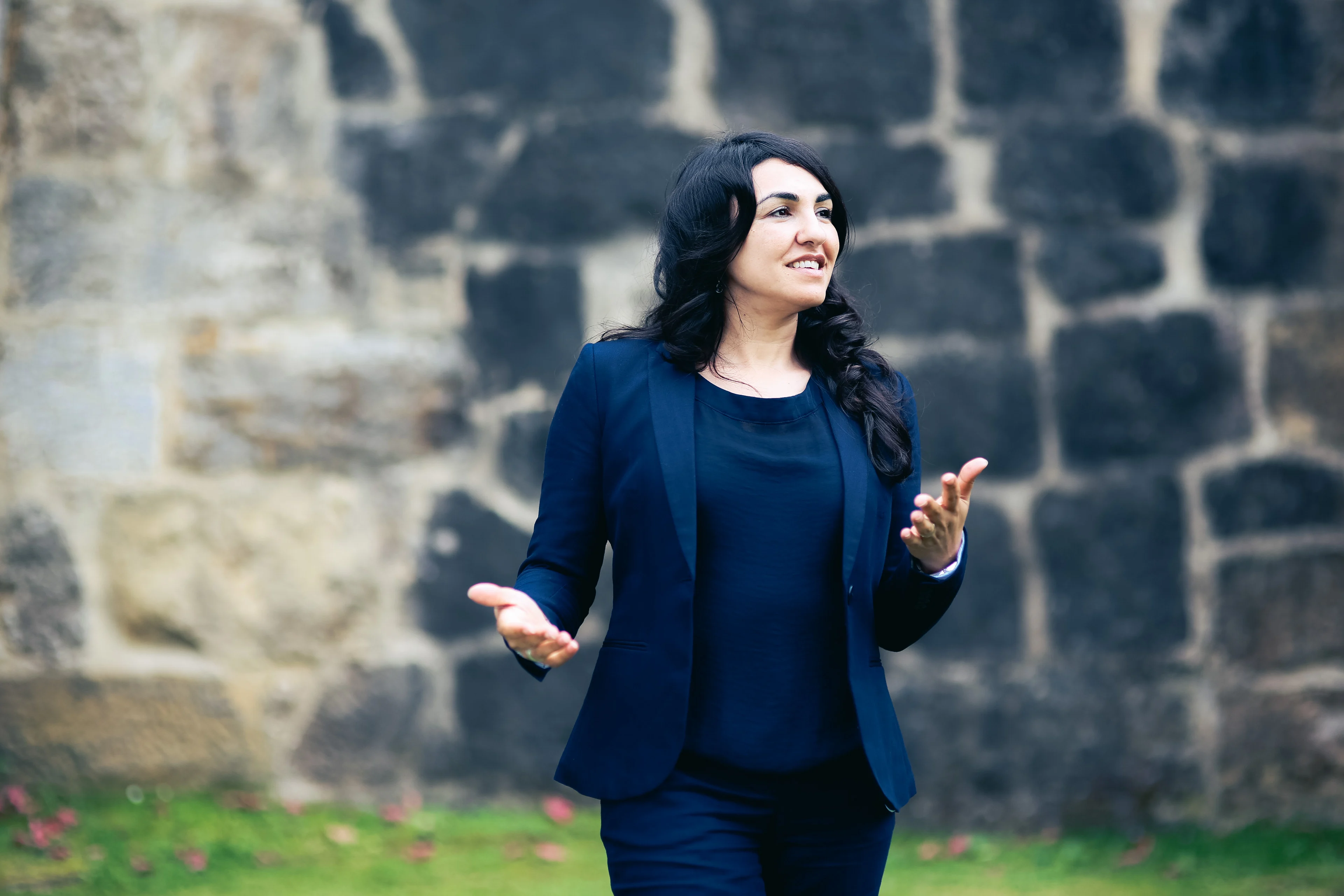 Asiye Balıkçı-Schmidt im Gespräch vor einer Natursteinmauer, mit offener Geste